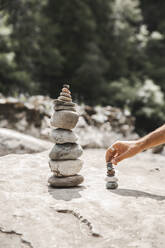 Hand eines Mannes, der Steine auf einem Felsen stapelt - PCLF00180