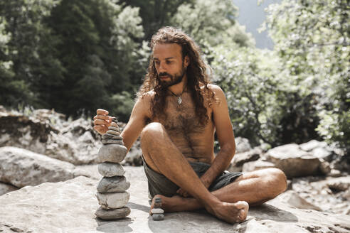 Shirtless young hipster stacking stones on rock - PCLF00181