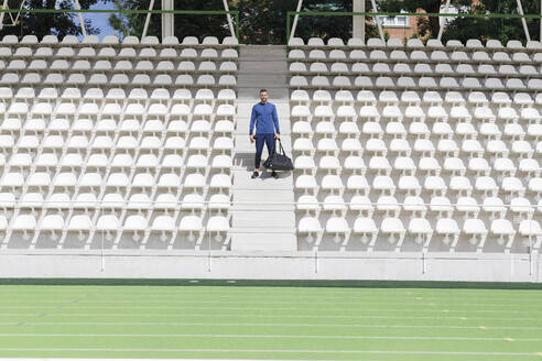 Sportler mit Tasche inmitten von Sitzen im Stadion stehend - IFRF01764