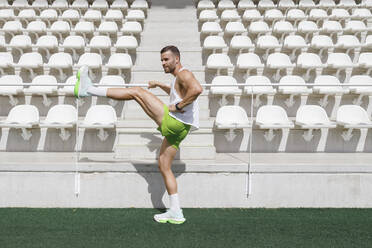 Man practicing warm up exercise at sports field on sunny day - IFRF01784