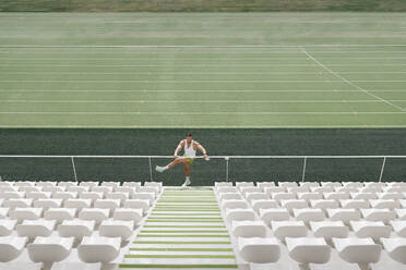 Sportsman doing warm up exercise on railing at stadium - IFRF01787