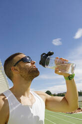 Athlete drinking water in front of blue sky on sunny day - IFRF01807