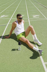 Tired athlete wearing sunglasses relaxing on sports track - IFRF01809