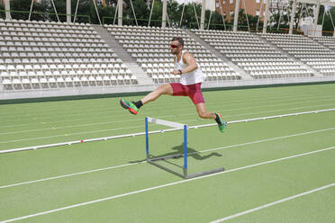 Athlete jumping over hurdle on sports track - IFRF01836