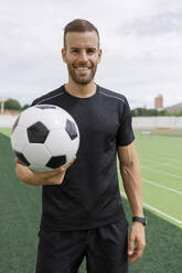 Smiling sportsman holding soccer ball on sports field - IFRF01840