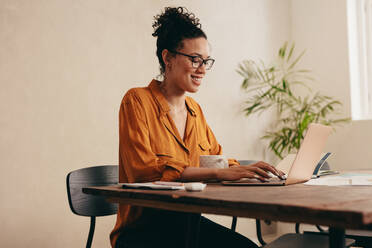 Woman working on laptop computer at home. Woman sitting at table with a coffee cup using a laptop at home office. - JLPSF08367