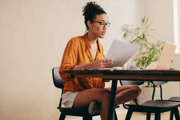 Businesswoman holding documents having a video conference call on her laptop. Woman working from home having a video call meeting. - JLPSF08369