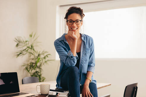 Porträt einer glücklichen jungen Frau, die mit einer Tasse Kaffee und einem Laptop auf dem Tisch sitzt. Frau sitzt im Büro zu Hause. - JLPSF08393