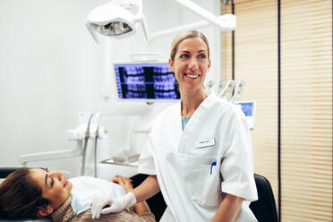 Happy female dentist looking away at something with a woman patient sitting on dentist's chair. Happy dentist and patient at dental clinic. - JLPSF08416