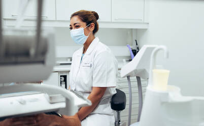 Eine Ärztin mit Gesichtsmaske sitzt in einer Klinik und untersucht einen Patienten. Eine Zahnärztin sitzt auf einem Stuhl und untersucht einen Patienten. - JLPSF08422