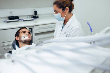 Female dentist in protective mask while treating a patient in dental office. Dental doctor talking with a smiling male patient sitting in dentist's chair. - JLPSF08423