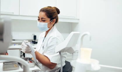 Dentist doing a dental treatment in teeth of a patient using tools. Female dental doctor wearing face mask working in her clinic. - JLPSF08426