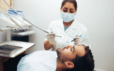 Ein Zahnarzt untersucht die Zähne eines Patienten auf dem Zahnarztstuhl in der Zahnklinik. Ein männlicher Patient wird in der Klinik zahnärztlich behandelt. - JLPSF08431
