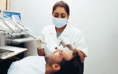 Female dentist examining teeth of a man in dental clinic using dental tools. Dentist inspecting teeth of male patient. - JLPSF08433