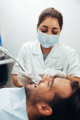 Ärztin bei der zahnärztlichen Behandlung eines Mannes auf dem Zahnarztstuhl. Zahnärztin mit Gesichtsmaske bei der Behandlung eines Patienten. - JLPSF08436