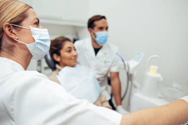 Eine Zahnärztin mit Gesichtsmaske zeigt einer Patientin eine Röntgenaufnahme. Ein Zahnexperte erklärt einer Patientin in der Klinik das Behandlungsverfahren. - JLPSF08444