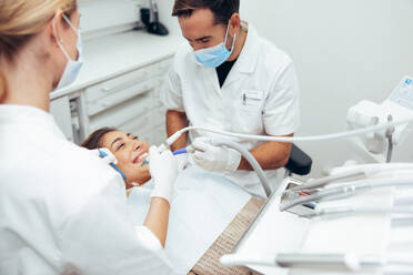 Dentist and his assistant examining the teeth of a female patient. Woman getting a dental treatment in clinic. - JLPSF08449