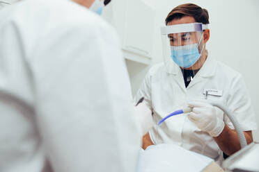 Männlicher Arzt bei der Arbeit an den Zähnen eines Patienten mit einem Assistenten im Vordergrund. Ein Zahnarzt behandelt einen Patienten in seiner Klinik. - JLPSF08453