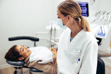 Zahnärztin mit Gesichtsmaske im Gespräch mit Patientin im Zahnarztstuhl. Zahnärztin mit Patientin bei Routineuntersuchung. - JLPSF08460