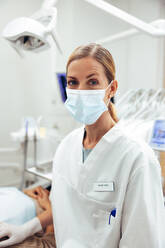 Portrait of a female dentist looking at camera. Dental doctor wearing protective face mask in her office. - JLPSF08463