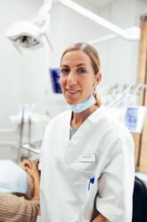 Porträt einer selbstbewussten Zahnärztin in ihrer Praxis, die in einen Laborkittel gekleidet in die Kamera schaut und lächelt. - JLPSF08464