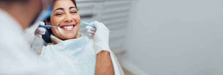 Glückliche Frau, die eine zahnärztliche Untersuchung in der Zahnarztpraxis erhält. Zahnarzt mit zahnärztlicher Ausrüstung zur Untersuchung der Zähne einer Patientin. - JLPSF08470