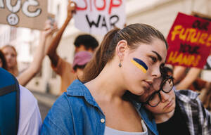 Beendigung des Konflikts in der Ukraine: Junge Frau, die mit der ukrainischen Flagge im Gesicht gegen den Krieg demonstriert. Gruppe multikultureller junger Menschen bei einer Anti-Kriegs-Demonstration in der Stadt. - JLPSF08503