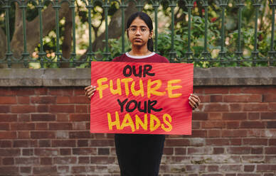 Junges Teenager-Mädchen, das in die Kamera schaut und ein Plakat zum Klimawandel in der Hand hält. Junge Umweltaktivistin, die gegen die globale Erwärmung und den Klimawandel protestiert. - JLPSF08515