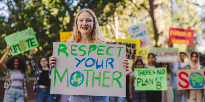 Happy youth activist smiling at the camera while leading a march against climate change. Group of multiethnic teenagers protesting against global warming. Teenagers joining the global climate strike. - JLPSF08524