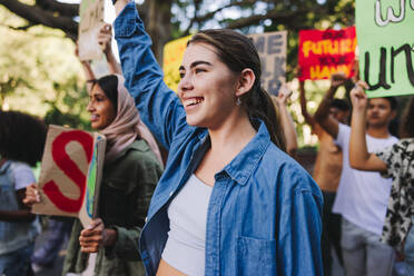 Happy young people standing up against climate change. Group of multiethnic youth activists carrying posters while marching against global warming. Diverse teenagers joining the global climate strike. - JLPSF08531