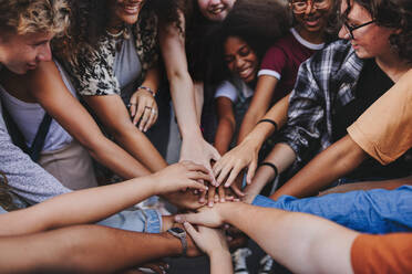 Happy teenagers putting their hands together in a huddle. Group of multicultural young kids stacking hands together in unity - JLPSF08563