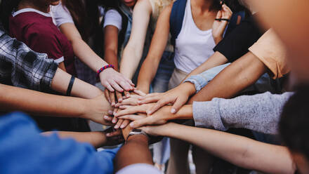 Multicultural teenagers putting their hands together in a huddle. Group of unrecognizable young people expressing their unity and teamwork - JLPSF08564