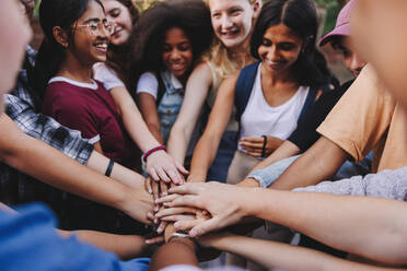 Fröhlich lächelnde Teenager, die sich die Hände reichen. Eine Gruppe multikultureller Studenten bildet einen Stapel Hände - JLPSF08565