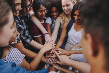 Diverse teenagers smiling happily while putting their hands together in a huddle. Group of multicultural young kids symbolizing unity and teamwork. - JLPSF08566