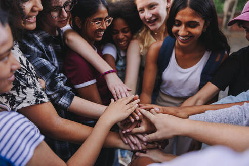 Group of multicultural teenagers smiling cheerfully while putting their hands together in a huddle. Happy young students stacking their hands in unity. - JLPSF08568