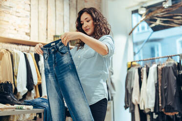 Frau betrachtet ein Paar Jeans in einem Modegeschäft. Weibliche Kundin kauft Jeans in einem Bekleidungsgeschäft. - JLPSF08617