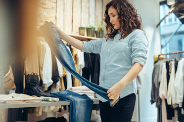 Woman looking at a quality of jeans in a clothing store. Shopper buying jeans in fashion store. - JLPSF08618