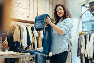 Frau hält Jeans und schaut weg, während sie im Geschäft einkauft. Frau kauft in einem Bekleidungsgeschäft ein. - JLPSF08619