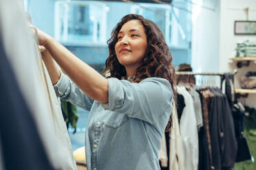 Female shopper in clothing store. Woman choosing clothes hanging on rack in fashion store. - JLPSF08620