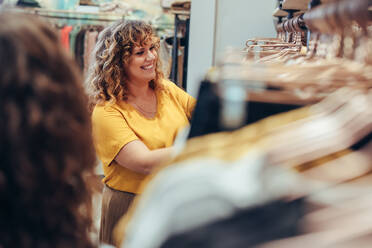 Lächelnder Shopper in einem Bekleidungsgeschäft, der Kleidung betrachtet. Frau betrachtet Kleidung, die in einem Modegeschäft hängt. - JLPSF08628