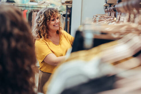 Smiling shopper in clothing store looking at clothes. Woman looking at clothes hanging in fashion store. - JLPSF08628