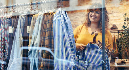 Eine Frau arbeitet in einem Bekleidungsgeschäft und hängt neue Kleidung auf ein Gestell im Laden. - JLPSF08632