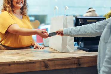 Female customer handing over her credit card to the cashier at clothing store. Shopper paying of her purchases with credit card. - JLPSF08638