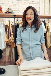 Lächelnde Einkäuferin in einem Modegeschäft: Frau, die in einem Bekleidungsgeschäft einkauft, schaut weg und lächelt. - JLPSF08647