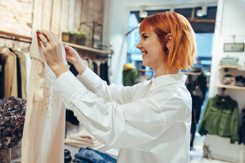 Woman holding a shirt and showing to customer in store. Fashion store owner assisting customer in shop. - JLPSF08655