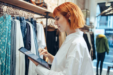 Woman using digital tablet in her clothing store. Fashion store owner checking the stock in her shop. - JLPSF08661