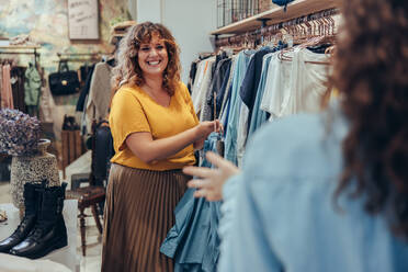 Verkäuferin hilft Käuferin bei der Auswahl von Kleidern in einem Modegeschäft. Inhaberin eines Bekleidungsgeschäfts hilft Kundin in ihrem Geschäft. - JLPSF08673