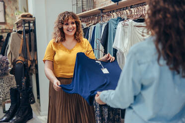 Angestellte eines Modegeschäfts hilft einer Kundin bei der Auswahl von Kleidung im Geschäft. - JLPSF08674