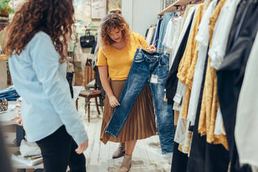 Fashion store owner showing a jeans to female customer. Shop assisting helping shopper in clothing store. - JLPSF08677