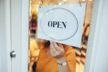 Frau hängt ein OPEN-Schild an die Tür ihres Geschäfts. Inhaberin eines kleinen Geschäfts, die ihr Geschäft öffnet. Nahaufnahme einer Frau, die ein Schild mit der Aufschrift 
